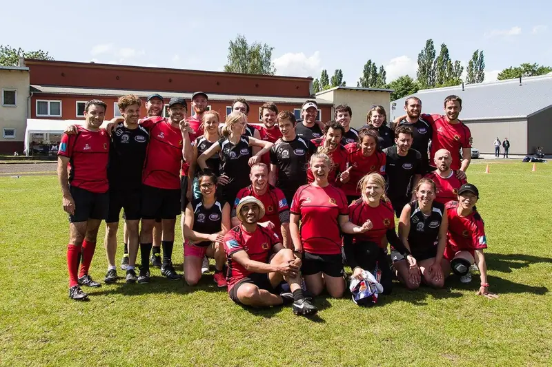 A mixed group of players stands together on a tree-lined pitch.